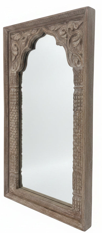 An ornate rectangular wooden mirror with intricate hand-carved floral and geometric patterns, standing on a dark wooden table inside a furniture showroom.