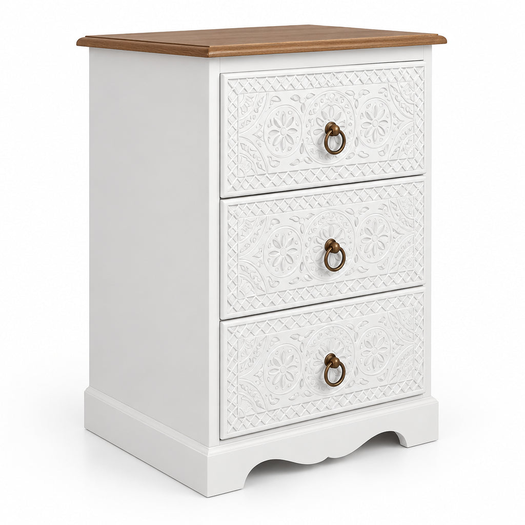 A three-drawer white bedside embossed floral patterns on the drawer fronts, a dark brown wooden top, and round metal ring pulls, shown against a plain off-white wall.