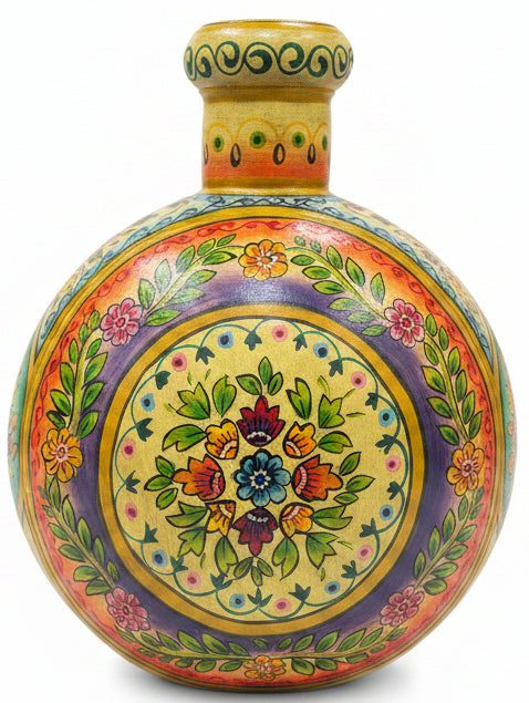 A round hand-painted wooden decorative vase with a narrow neck, featuring intricate multicolor floral and leaf patterns on a yellow background, set on a dark wooden table in a shop interior.