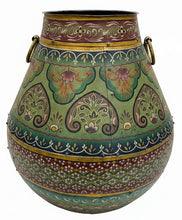 A large decorative hand-painted metal pot with intricate floral and paisley patterns in green, gold, red, and blue, set on a gray floor in a rustic shop environment.