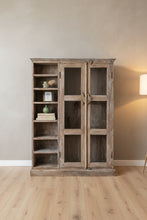 A rustic, distressed wooden bookcase and cabinet with two glass-paneled doors and open shelves on the left, photographed in a cluttered workshop or storage room.