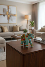 A hand-painted decorative elephant figurine in light blue with colorful traditional patterns, displayed on a wooden table in a shop setting.