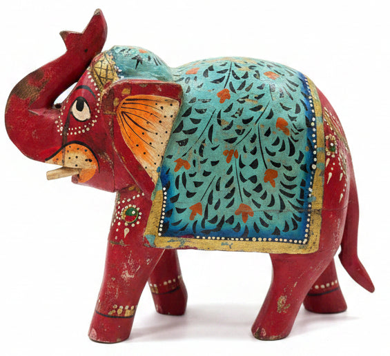 A hand-painted wooden elephant figurine with a red body and a turquoise blue patterned saddle, displayed on a wooden table in a shop.