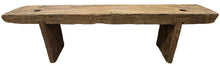 A rustic wooden bench with a thick, weathered plank top and block-style legs, positioned in front of a distressed gray cabinet on a concrete floor.
