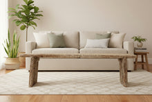 A rustic, weathered wooden bench with a thick rectangular seat and blocky legs, positioned in front of a matching carved wooden chest in what appears to be a shop or storage room.