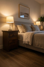 A rustic three-drawer wooden nightstand or end table with dark metal ring pulls, photographed in a warehouse setting with cardboard boxes in the background.