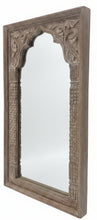 An ornate rectangular wooden mirror with intricate hand-carved floral and geometric patterns, standing on a dark wooden table inside a furniture showroom.