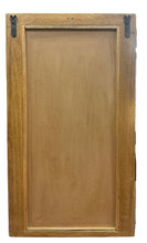 A rectangular wooden cabinet door or panel with a recessed center panel and dark metal hardware, standing on a wooden table in a furniture store.