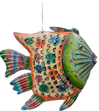 A large, colorful hand-painted fish sculpture or decorative fish figure displayed on a wooden table inside a shop. The fish features a cream-colored body with orange, blue, and green painted scales, a green head with blue stripes, and multicolored fins.
