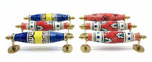 Six decorative cabinet pulls with ornate hand-painted ceramic handles and brass hardware, arranged diagonally on a dark wooden table.