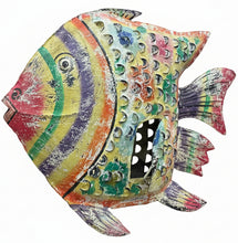 A large, hand-painted metal fish sculpture with a vibrant rainbow pattern and textured shell details, displayed on a dark wooden table inside a home decor store.