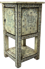 A small carved wooden side table or cabinet with two front panels decorated with elephant motifs, shown in a shop setting on a gray floor.
